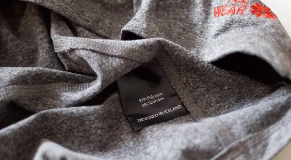 Szara koszulka z metką "92% Polyester 8% Spandex". Czy poliester się gniecie? Ta tkanina wygląda na odporną na zagniecenia.