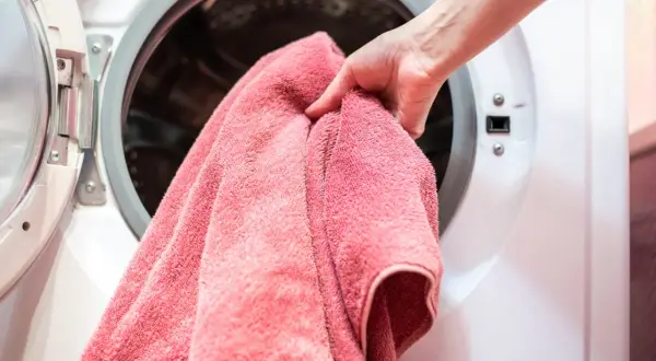 Dłoń wkłada różowy ręcznik do pralki. Zastanawiasz się, w jakiej temperaturze prać ręczniki, by były czyste i miękkie.