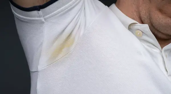 Widoczne plamy potu pod pachami na białej koszulce polo.
