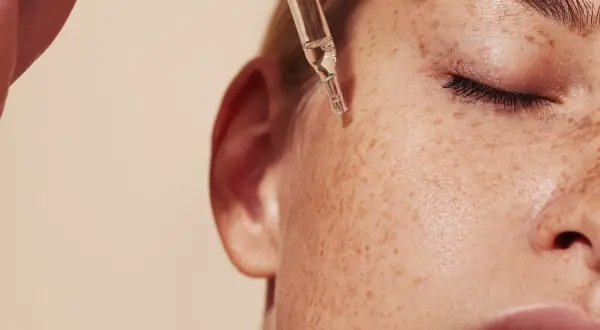 Kropla serum z pipetki spada na piegowatą skórę. Dowiedz się, jak stosować retinol dla pięknej cery.