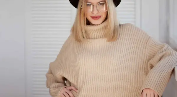 Kobieta w beżowym swetrze oversize i okularach, prezentująca stylowe, luźne ubrania.