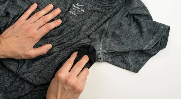 Dłonie czyszczą ciemną koszulkę Nike, by pozbyć się zapachu potu. Skuteczny sposób na świeżość ubrań sportowych.