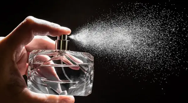 Dłoń trzyma szklaną buteleczkę, z której rozpyla się mgiełka. To woda perfumowana, lekka jak perfumy.