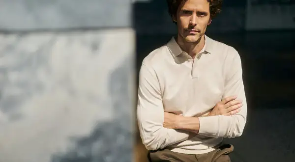 Mężczyzna w beżowym longsleeve polo z długim rękawem, z rękami skrzyżowanymi na piersi.