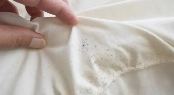 Dłoń pokazuje biały materiał z widocznymi, nieestetycznymi, tłustymi plamami na ubraniach po praniu.