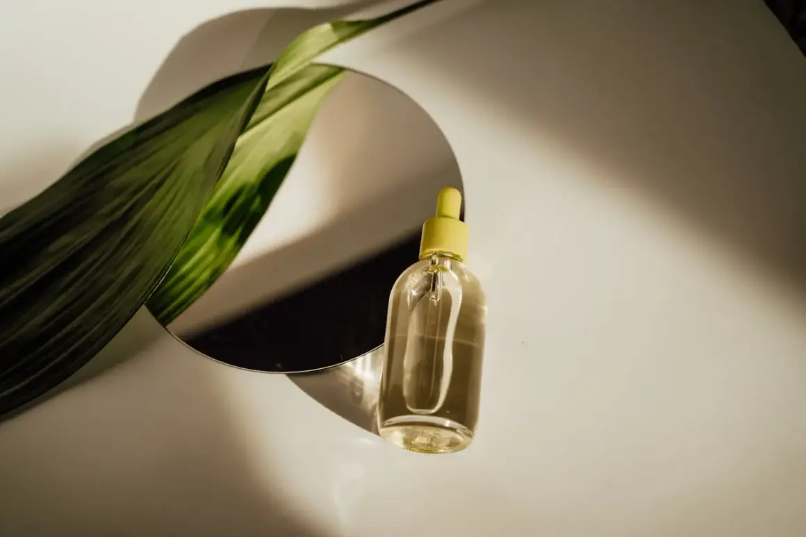Szklana buteleczka z żółtą pipetką i zielony liść odbijają się w lustrze. Czy serum się zmywa? Naturalne piękno w kropli.