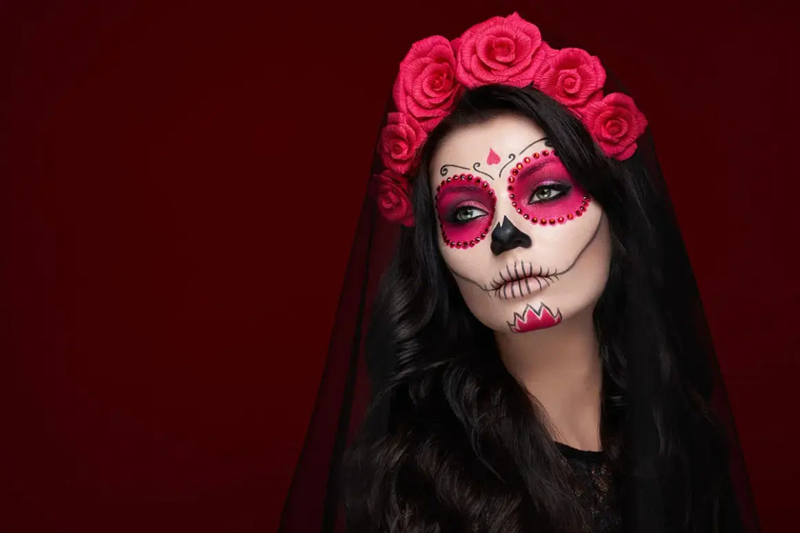 Kobieta z delikatnym makijażem na Halloween w stylu Catriny, ozdobiona czerwoną opaską z róż.