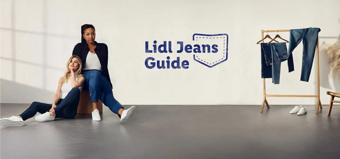 Dwie kobiety w jeansach siedzą na podłodze. Obok wieszak z jeansami. Rozmiar 27 jaki to rozmiar? Sprawdź w Lidl Jeans Guide.