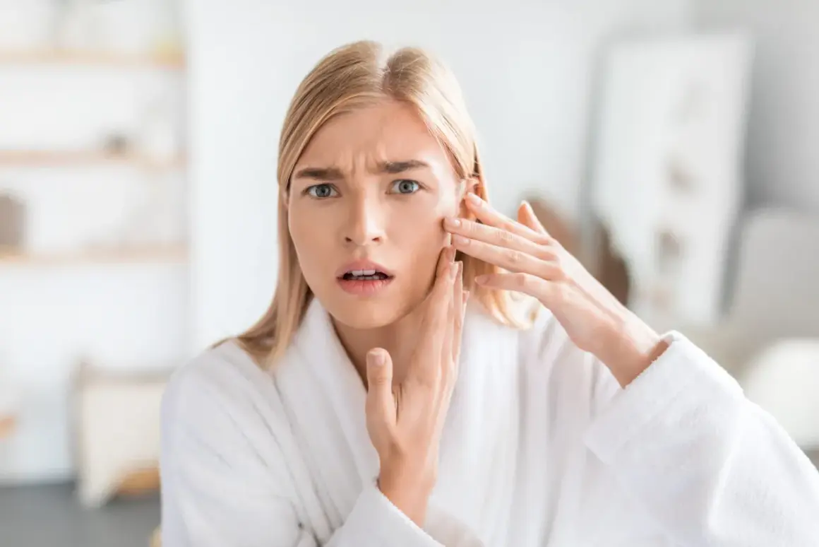 Zmartwiona kobieta w szlafroku sprawdza swoją cerę suchą, szukając skutecznej pielęgnacji.