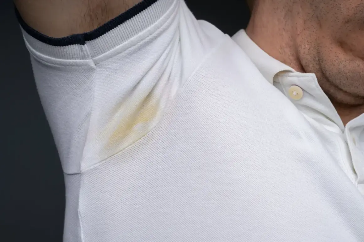 Widoczne plamy potu pod pachami na białej koszulce polo.