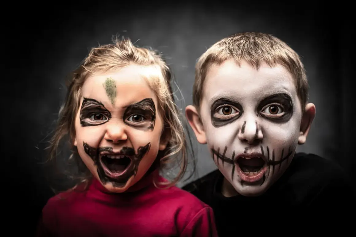 Dwoje dzieci z przerażającymi makijażami na Halloween. Dziewczynka ma zieloną plamę na czole i czarne wzory wokół oczu. Chłopiec ma białą twarz z czarnymi szwami na ustach. To łatwy makijaż na Halloween dla dzieci.