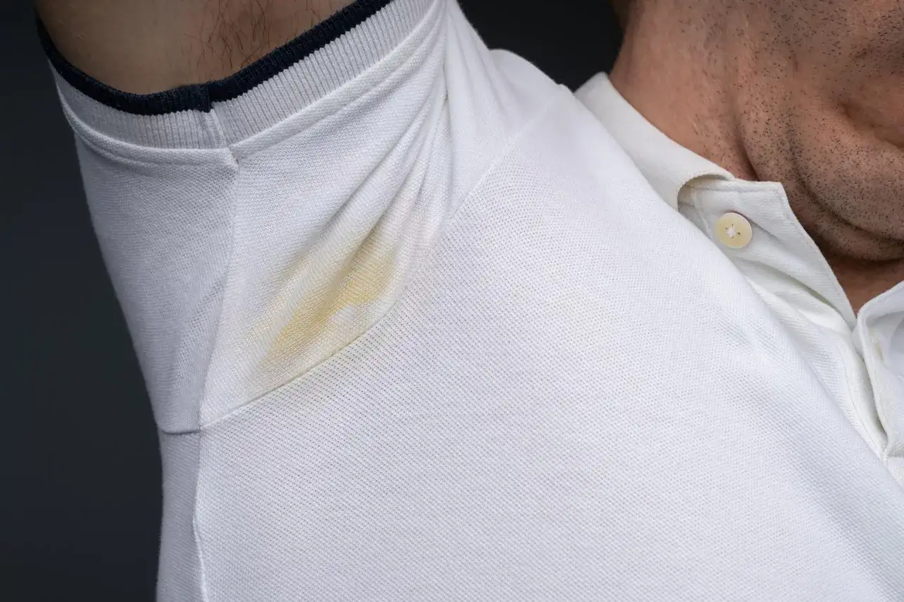 Widoczne żółte plamy potu pod pachami na białej koszulce polo.