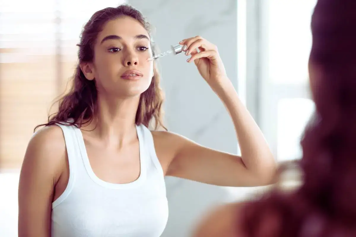 Kobieta aplikuje serum z pipetki na policzek, pokazując, jak stosować retinol dla pięknej cery.