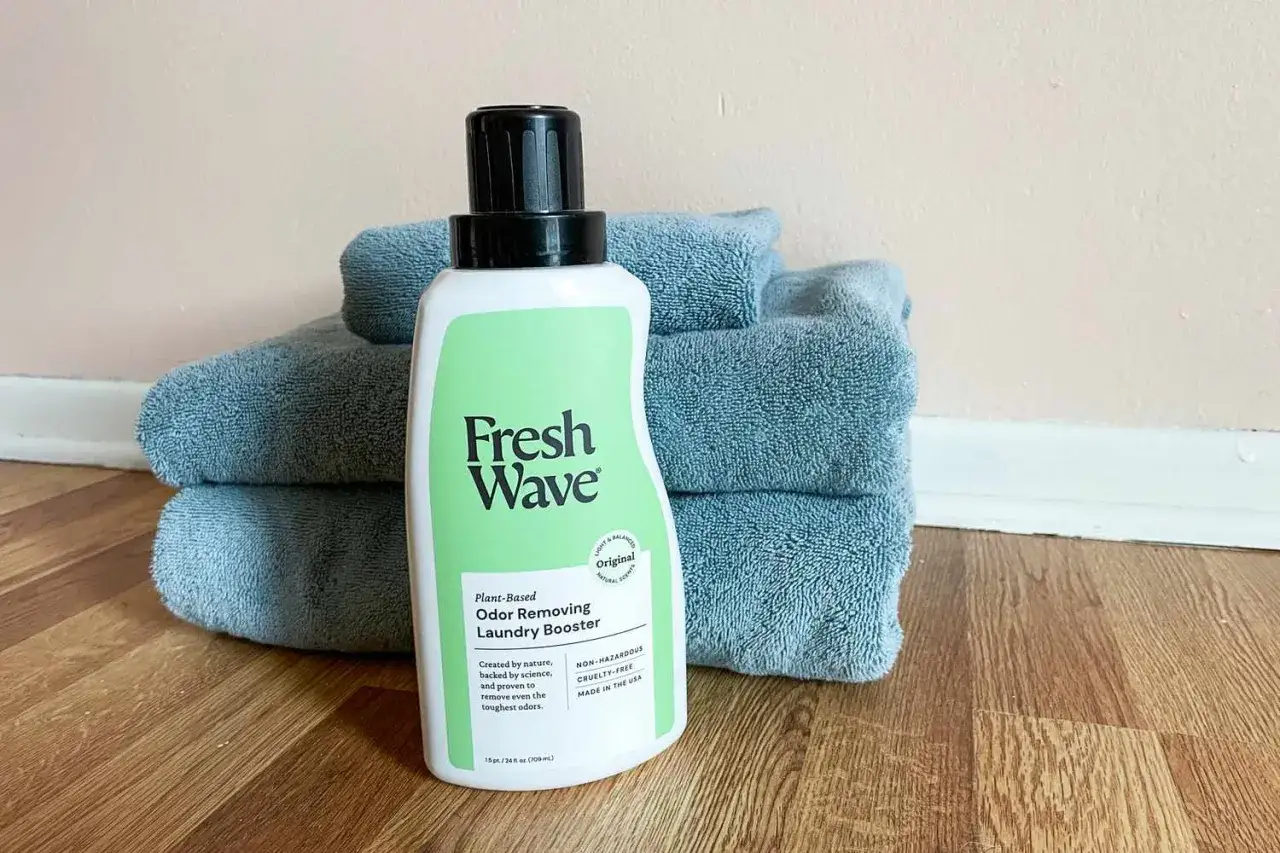 Butelka Fresh Wave Laundry Booster i stos ręczników. Skuteczny sposób, jak pozbyć się zapachu potu z ubrań.