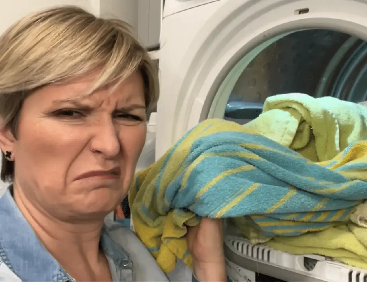 Kobieta z grymasem na twarzy obok suszarki z mokrym praniem. Zastanawia się, dlaczego pranie śmierdzi po wysuszeniu.