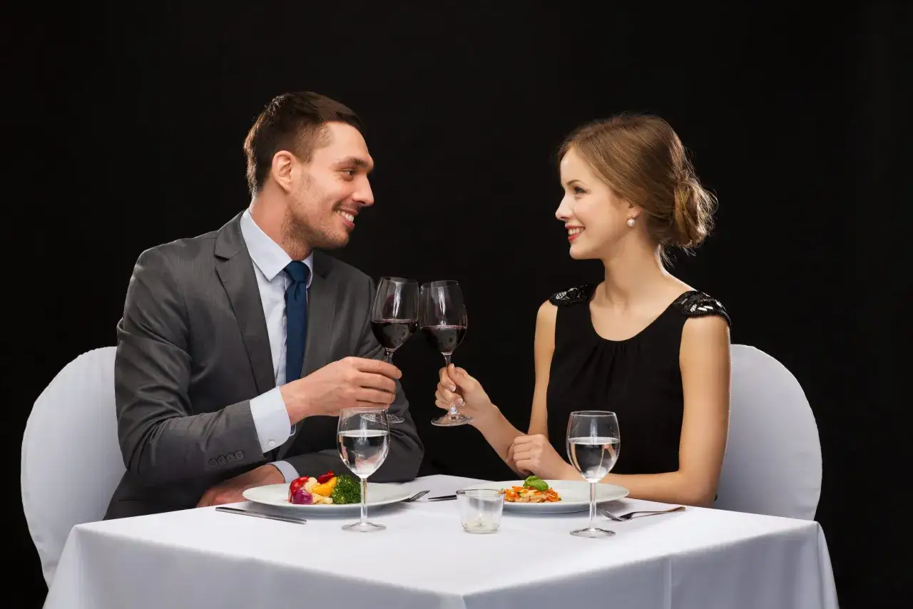 Elegancka stylizacja do restauracji: para wznosi toast kieliszkami czerwonego wina, siedząc przy nakrytym stole.