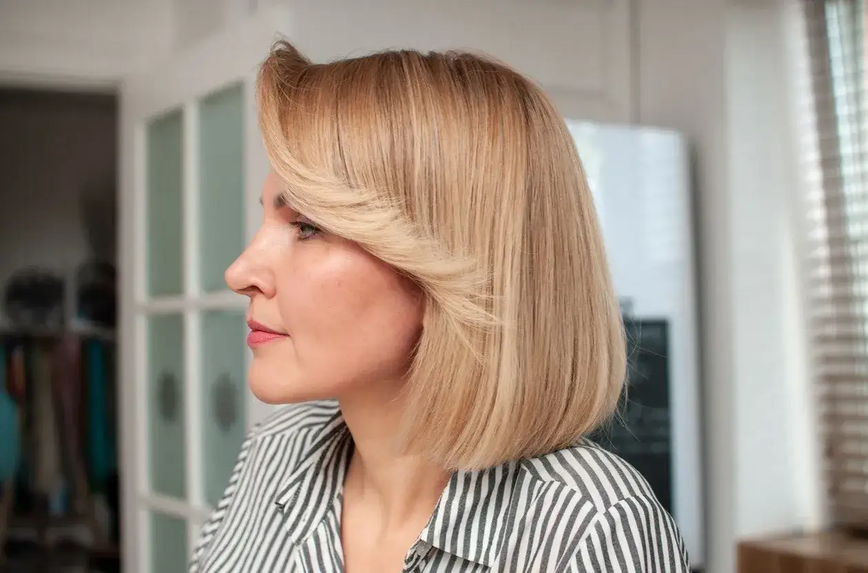 Kobieta z blond włosami w stylu long bob z grzywką, patrząca w bok.