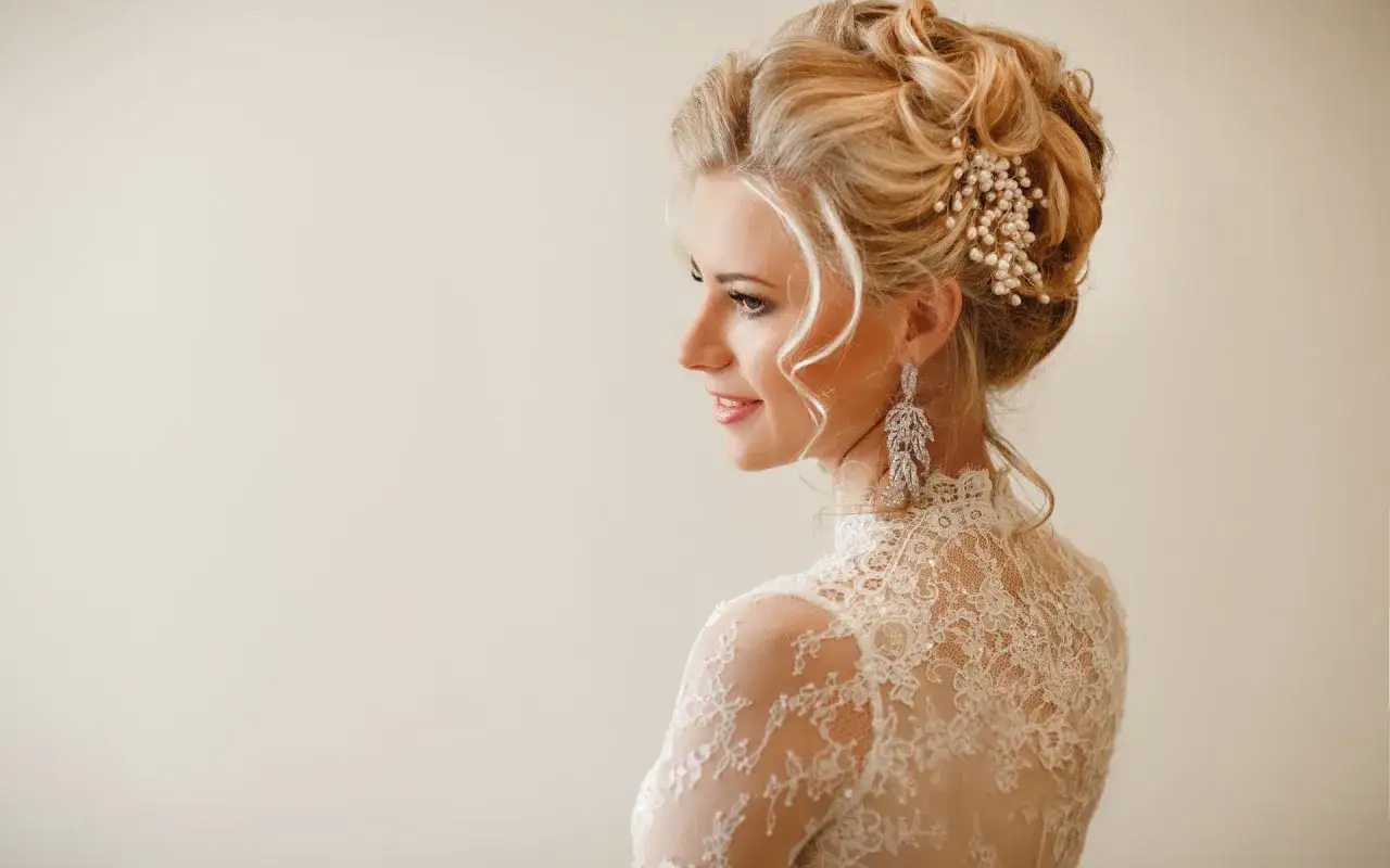 Eleganckie fryzury na wesele dla średnich włos&oacute;w: upięcie z perłami i długimi kolczykami.