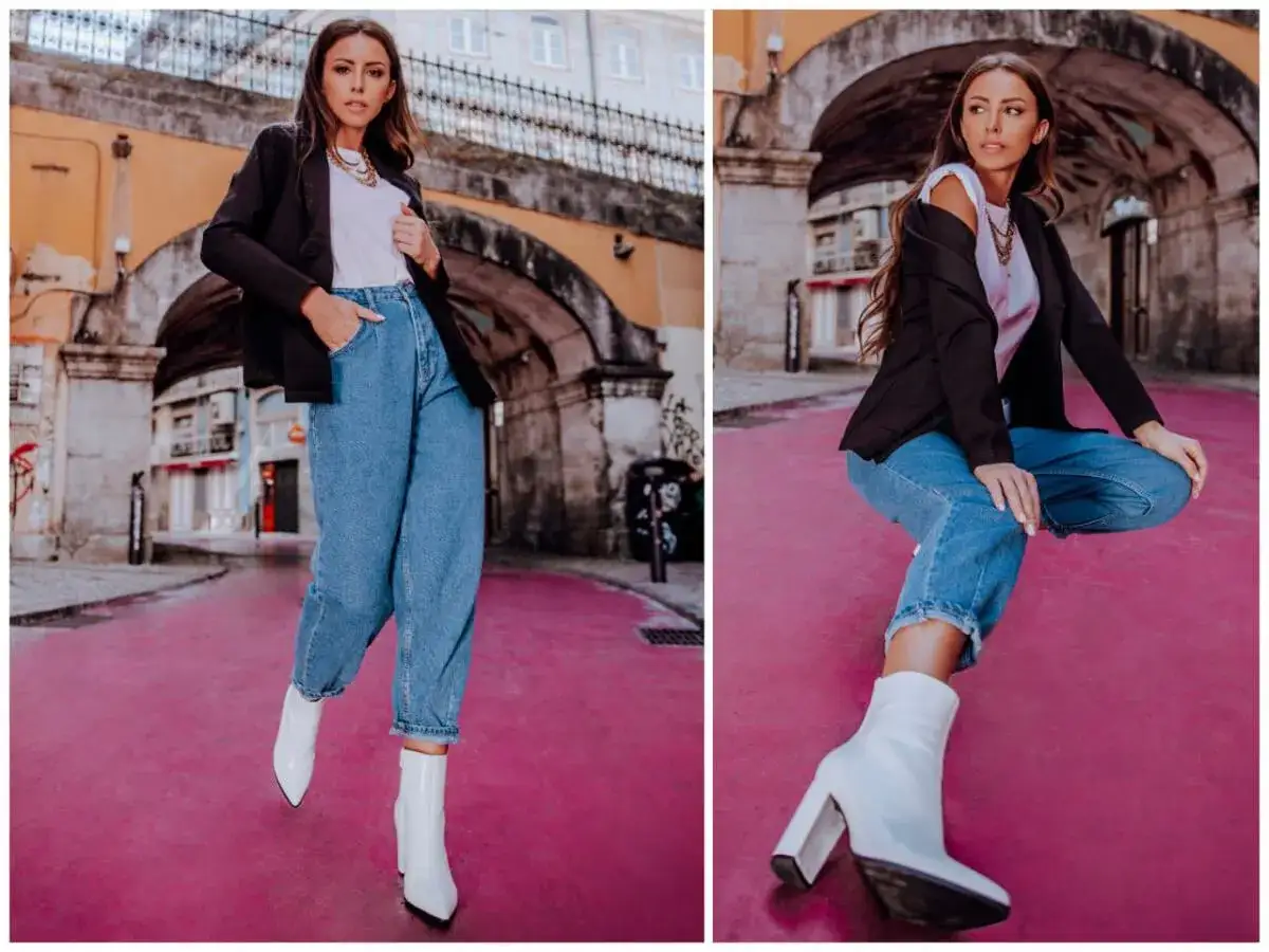 Kobieta w modnych spodniach mom fit i białych kozaczkach na różowym tle.