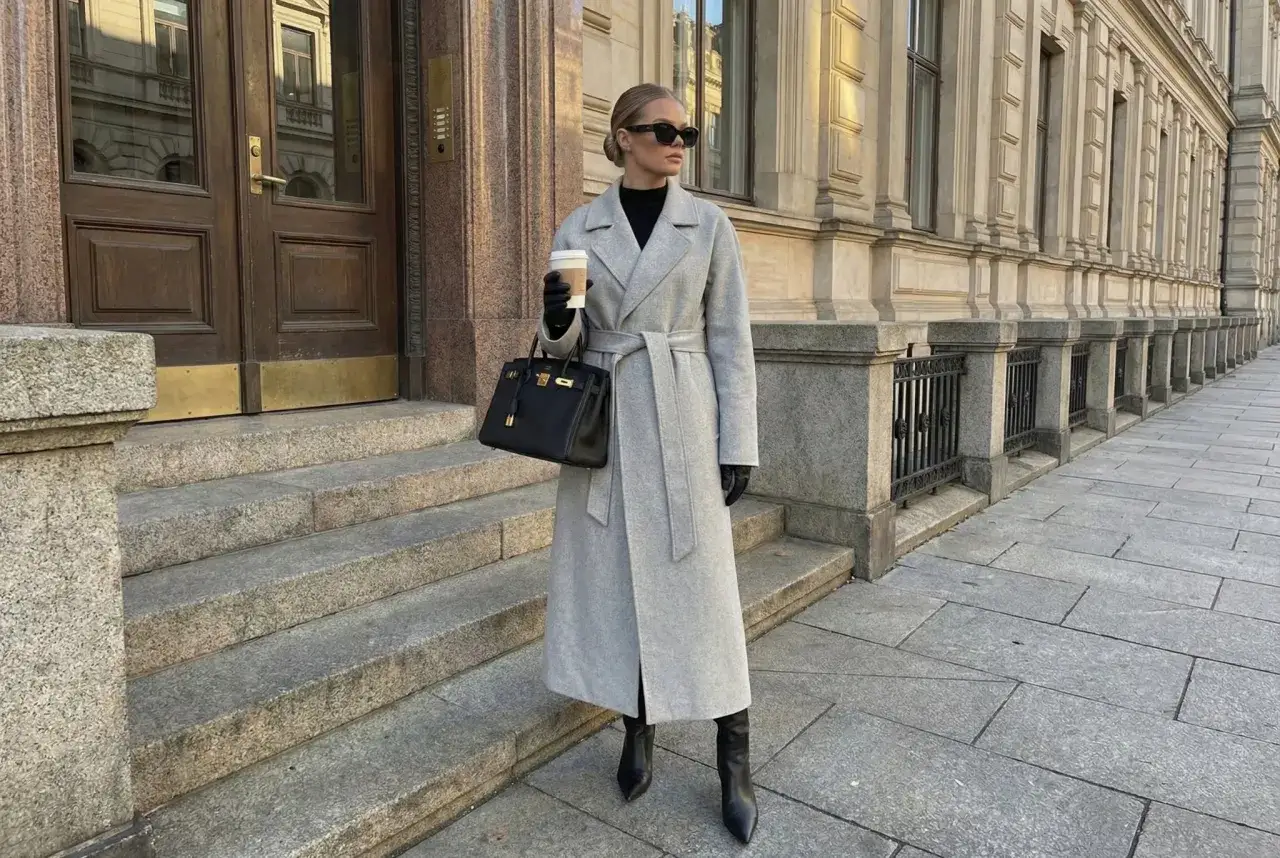 Eleganckie stylizacje z płaszczem: szary, długi płaszcz wiązany w pasie, czarna torebka i skórzane kozaki.