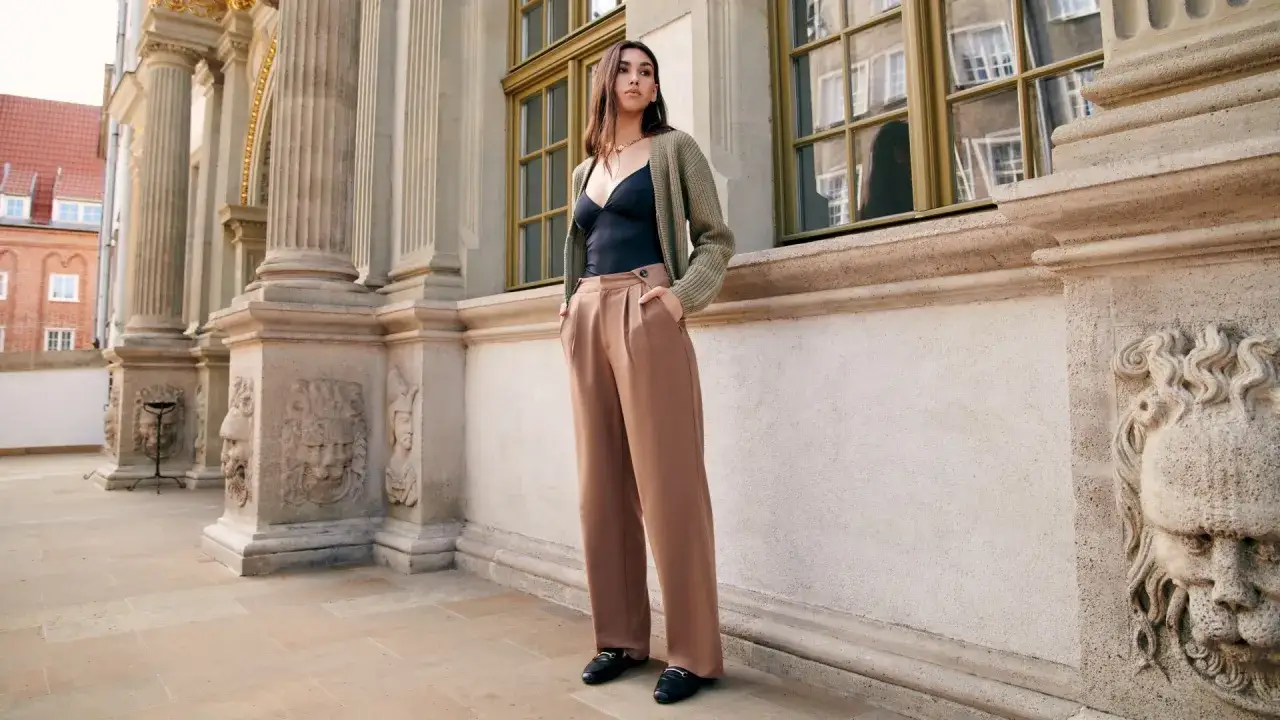 Elegancka kobieta w brązowych, szerokich spodniach i czarnych mokasynach. Idealne połączenie, by odpowiedzieć na pytanie: jakie buty do szerokich eleganckich spodni.