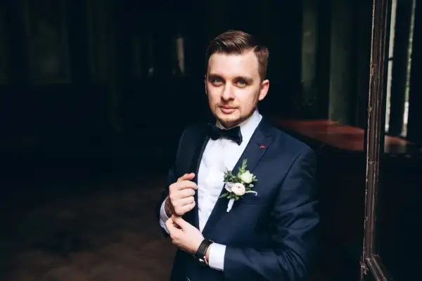 Elegancki mężczyzna w granatowym garniturze, z butonierką i muszką. Idealny przykład, jak dobrać garnitur na specjalną okazję.