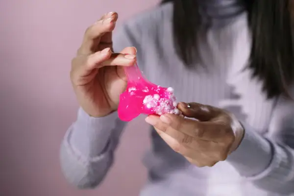 Różowy slime z białymi kuleczkami w dłoniach. Dowiedz się, jak usunąć slime z ubrania, zanim zaschnie.