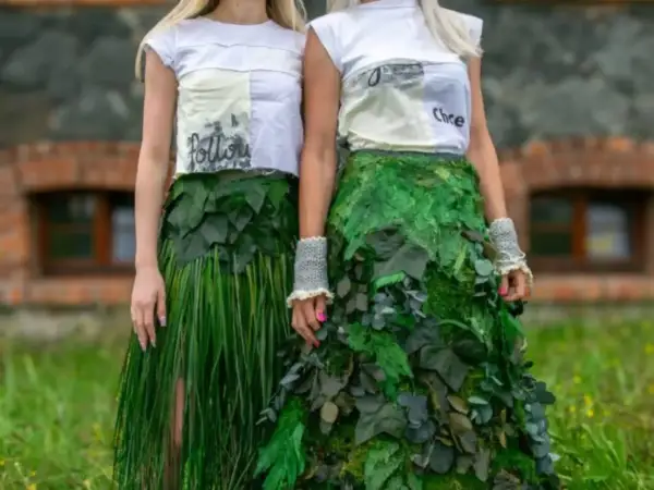 Dwie kobiety prezentują ekologiczną modę z recyklingu. Jedna w spódnicy z trawy, druga w sukni z liści.