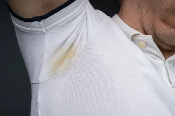 Widoczne plamy potu pod pachami na białej koszulce polo.