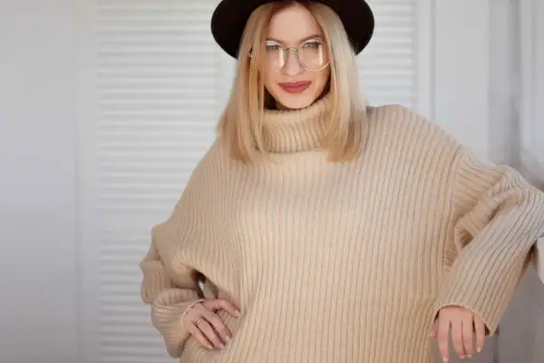 Kobieta w beżowym swetrze oversize i okularach, prezentująca stylowe, luźne ubrania.