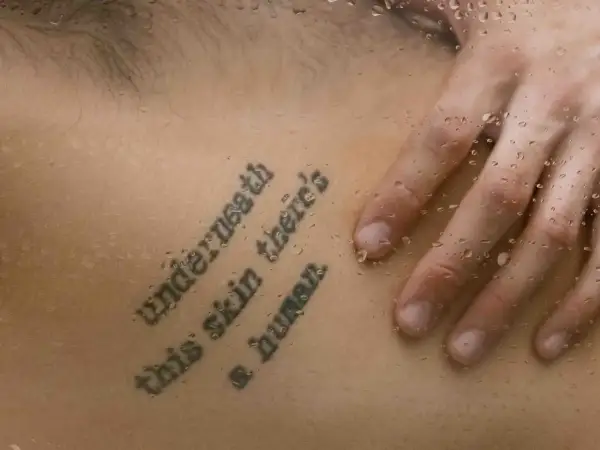 Mądre cytaty na tatuaż: "Underneath this skin there's a human". Dłoń na skórze z kroplami wody.